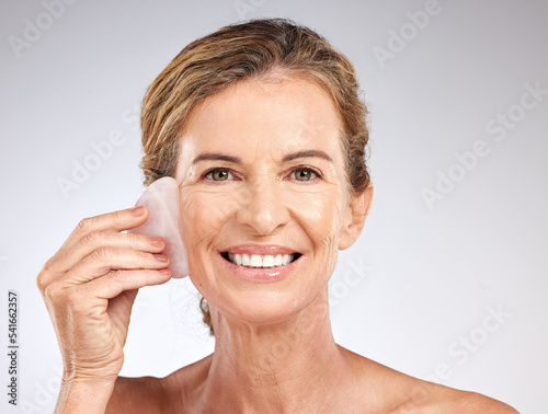 Face, beauty and senior woman with stone for facial massage on gray studio background. Health, skincare and elderly female model from Canada with rose quartz guasha for anti aging or smooth wrinkles