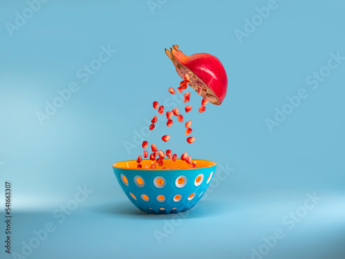 Halved pomegranate with pomegranate seeds falling into a bowl that looks like a pomegranate photo