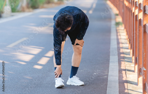Asian young man is suffering from ankle ache when exercising outdoors.