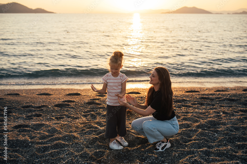 Mother and daughter having fun on the beach at sunset.