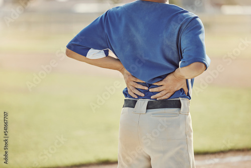 Sports, baseball injury and man with back pain, emergency or muscle strain during game, competition or fitness match. Softball player, field pitch or back view of athlete with hurt spine or backache photo