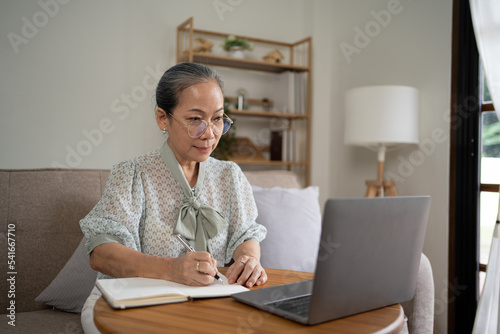 Relaxed Elderly Woman Spending Time With Digital Tablet On Couch In Living Room  Browsing Internet Or Reading News  Side View