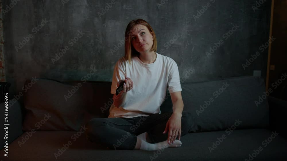 A young red-haired woman is sitting on the couch and can't choose what to watch on TV A young red-haired woman is sitting on the couch and can't choose what to watch on TV