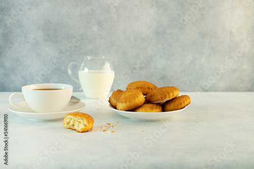 Delicious snack: a cup of black tea with milk and a plate of cookies on a gray background.