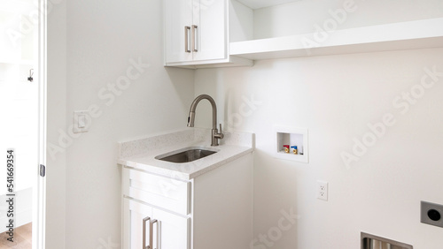 Panorama Empty laundry room with single vanity sink, wall cabinets and shelves