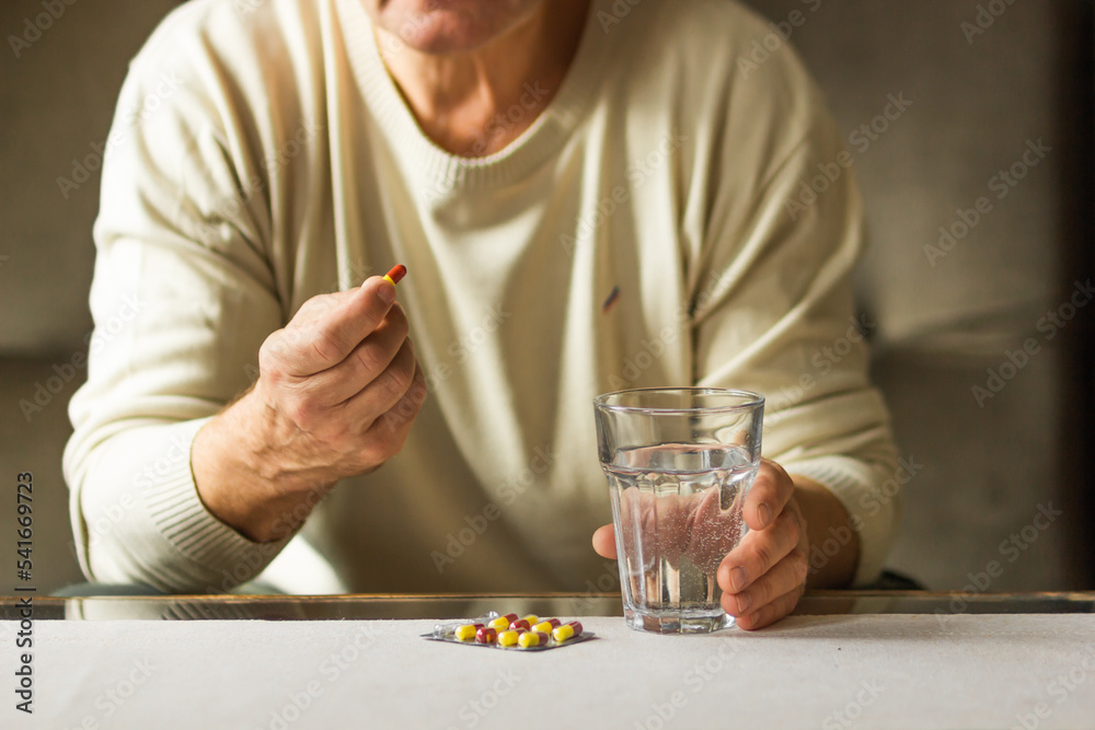 Senior man's hands holds red and yellow capsule and glass of water over the table, ready to take medicines. Health care. Senior man's hands holds red and yellow capsule and glass of water over the table, ready to take medicines. Health care.