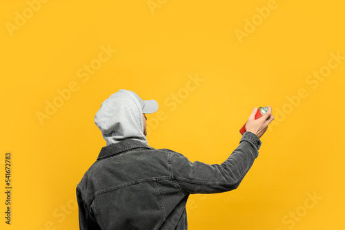 Man holding can of spray paint on yellow background, back view
