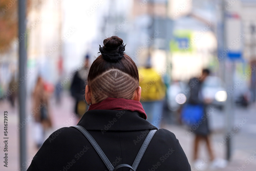 Girl with a shaved nape walking down the autumn street. Fashionable female haircut with patterns