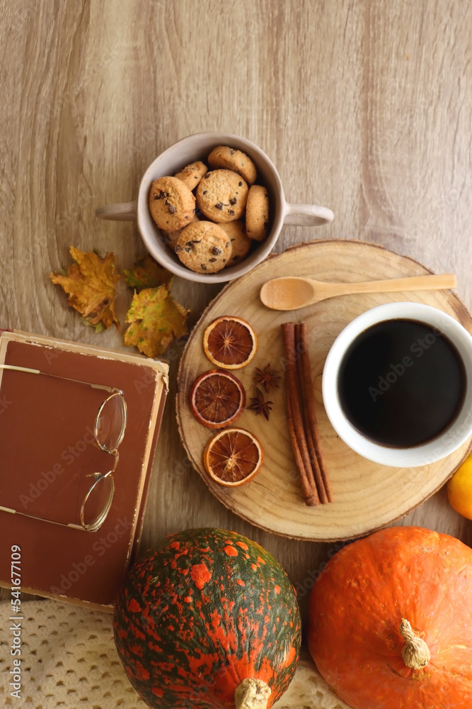 Cup of tea or coffee, seasonal spices, bowl of cookies, blanket, pumpkins, colorful leaves, books and tangerines on wooden table. Cozy hygge at home. Top view.
