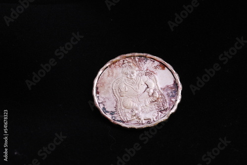 Close of a silver coin engraved with images of Kuberan, god of money isolated in black background photo