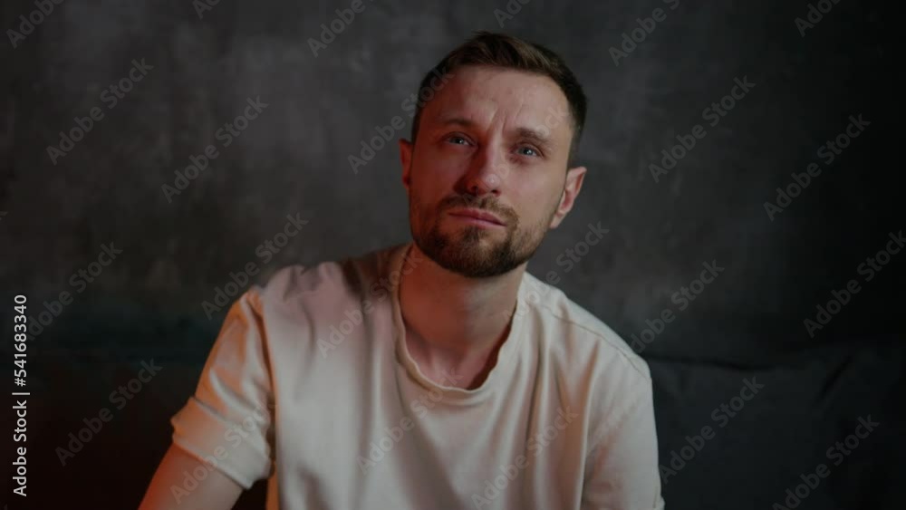 A man in a white t-shirt switches channels while sitting on the couch in front of the TV. Evening pastime at home A man in a white t-shirt switches channels while sitting on the couch in front of the TV. Evening pastime at home