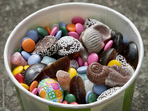 Closeup shot of a paper cup filled with chocolates and candies of various forms and colors