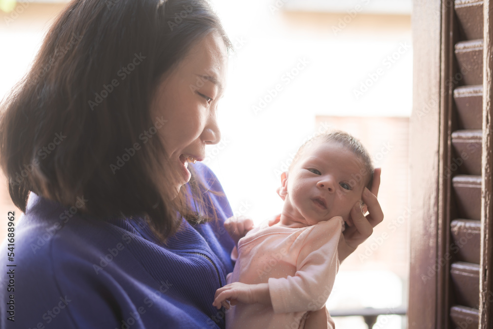 lifestyle shot on young and happy Asian Chinese woman holding tenderly her adorable newborn baby girl in her arms in mother and daughter love and care concept lifestyle shot on young and happy Asian Chinese woman holding tenderly her adorable newborn baby girl in her arms in mother and daughter love and care concept