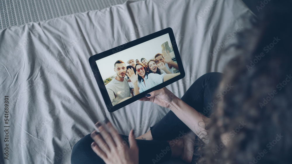 Dark-haired girl is talking with friends online using tablet looking at display, gesturing and waving hand. Modern technology, chat with friends and happy millennials concept. Dark-haired girl is talking with friends online using tablet looking at display, gesturing and waving hand. Modern technology, chat with friends and happy millennials concept.