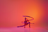 Studio shot of young charming girl, rhythmic gymnast training with sports equipment isolated over pink background in neon light filter