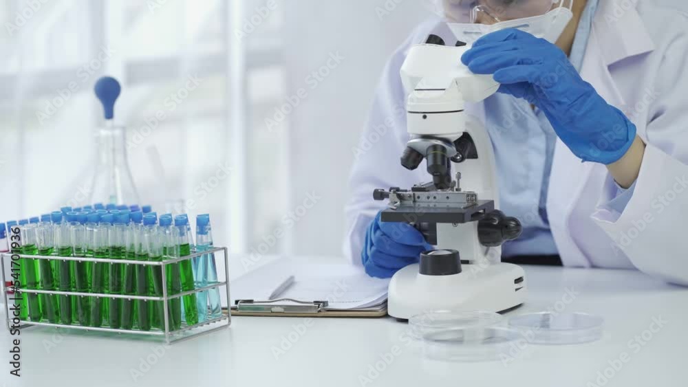A female scientist doing chemistry experiments in a laboratory.A beautiful woman doctor in a hat and mask pours a solution from a test tube onto a glass bottle containing red and green liquid. A female scientist doing chemistry experiments in a laboratory.A beautiful woman doctor in a hat and mask pours a solution from a test tube onto a glass bottle containing red and green liquid.