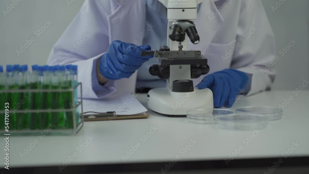 A female scientist doing chemistry experiments in a laboratory.A beautiful woman doctor in a hat and mask pours a solution from a test tube onto a glass bottle containing red and green liquid. A female scientist doing chemistry experiments in a laboratory.A beautiful woman doctor in a hat and mask pours a solution from a test tube onto a glass bottle containing red and green liquid.