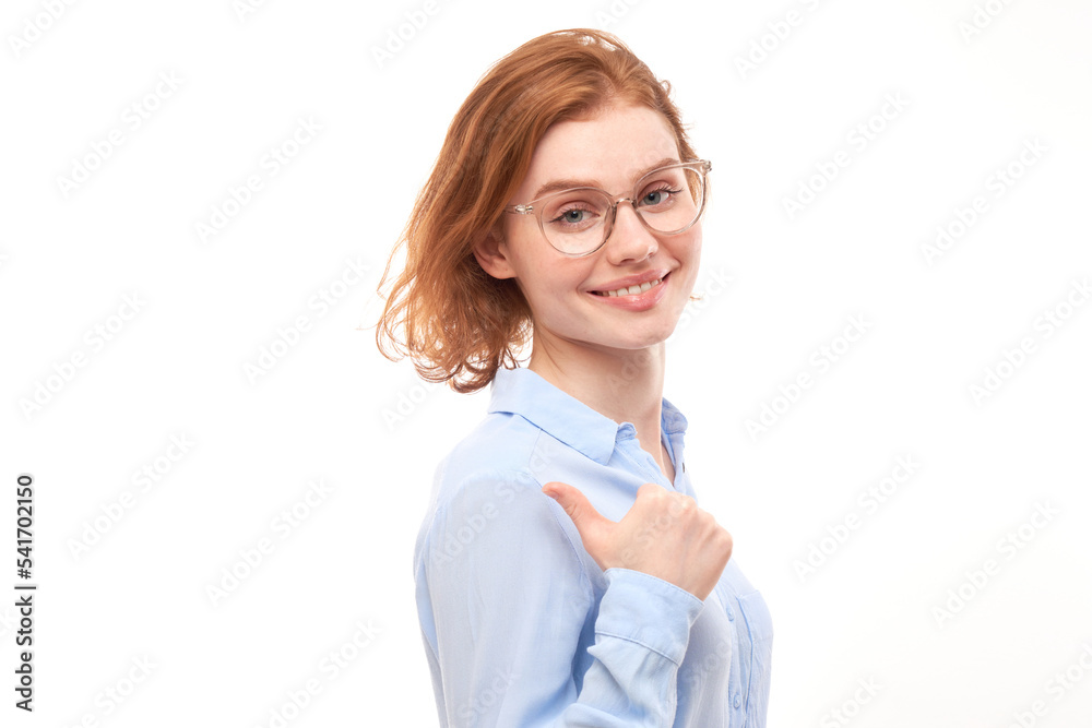 Portrait of a positive redhead young woman in a business shirt smiling pointing her finger at the empty copy space for text or product isolated on white background, advertising banner Portrait of a positive redhead young woman in a business shirt smiling pointing her finger at the empty copy space for text or product isolated on white background, advertising banner