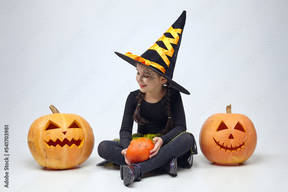 Fototapeta premium portrait of a charming little girl in a witch costume, Jack's lamps are standing around. the concept of the heluin holiday
