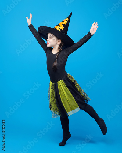 charming little girl in a witch costume dancing in the studio on a blue background