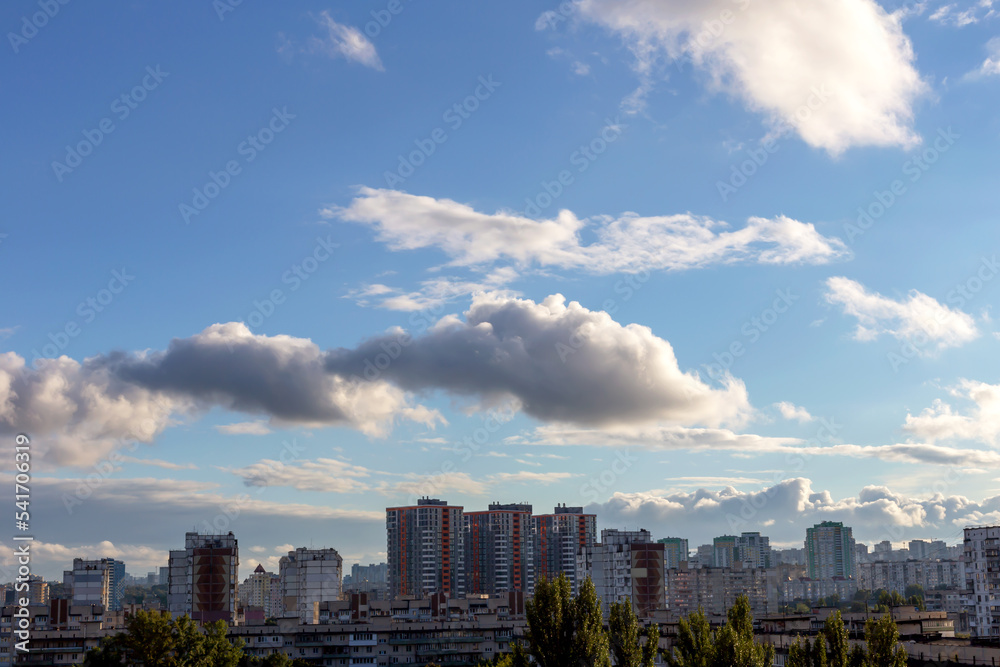 Beautiful fluffy cumulus clouds in the light blue sky above the city