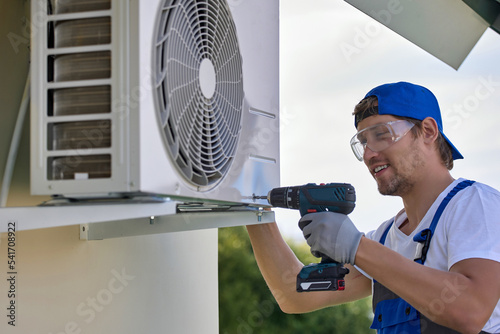 Quadro su tela Smiling caucasian worker installs the outer metal case of the air conditioner with a screwdriver
