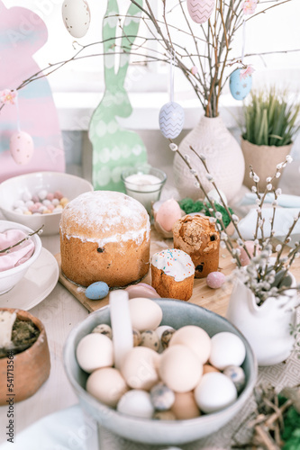 happy easter and spring holidays time. festive tablescape set decor. traditional dinner food easter eggs and baked cakes on table at home. rabbit and willow. pale pop pastel blue and pink color