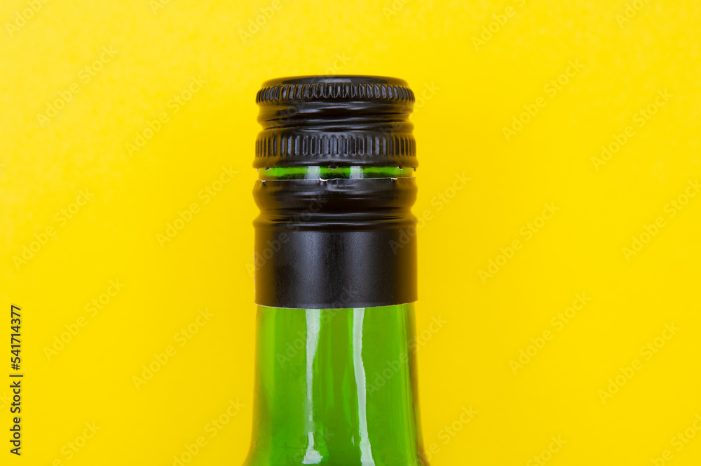 Glass wine bottle neck with cap close up on a yellow background