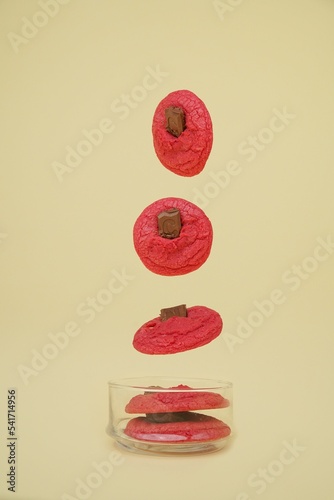 Pink cookies with chocolate falling in a transparent jar, vertical