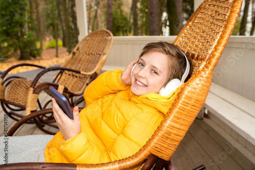 happy handsome child sits on rocking chair outside in autumn and listens to his favorite music in headphones