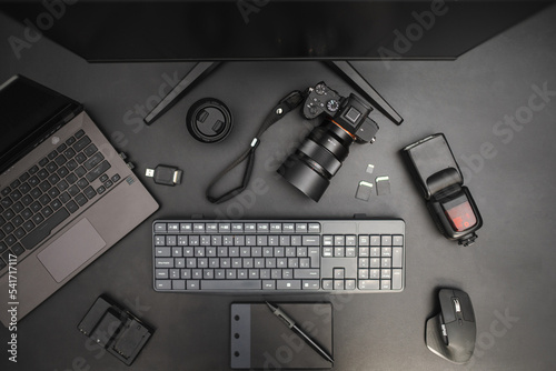 Photographer work station on dark background with laptop, camera, flash, lens, drawing tablet. Top view