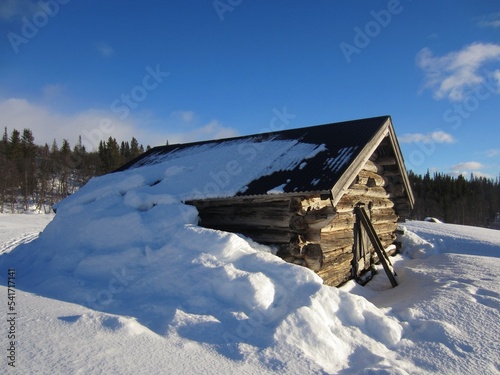 Old wooden cabin on a sunny day in norwegian mountains covered with snow. The snow has fallen from the roof.
