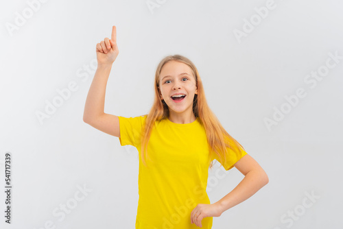 Enthusiastic teen girl smiling, pointing finger up, showing promo offer, way to store, banner or logo, standing in blank yellow tshirt over white background © AstiMak