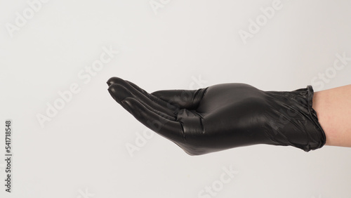 The hand is wearing a black latex glove and do beg hand sign on white background.