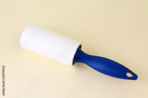 Cloth fabrics cleaner lint roller brush with paper roll blue grip on yellow color background. sticky roller, pet cat dog fur dust hair remover. Close-up