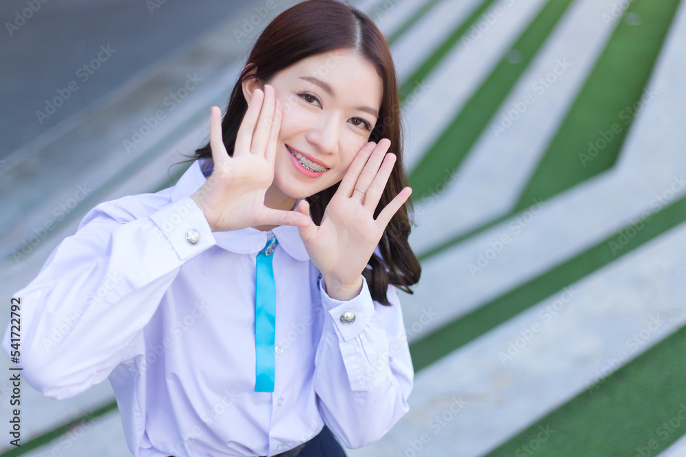 Beautiful high school Asian student girl in school uniform stands and smiles happily with braces on her teeth. Beautiful high school Asian student girl in school uniform stands and smiles happily with braces on her teeth.
