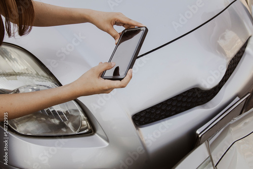 Young woman uses smartphone to record photo of the car's registration plate during a road accident to keep as evidence of car insurance to make an insurance claim : Accident and car insurance concept.