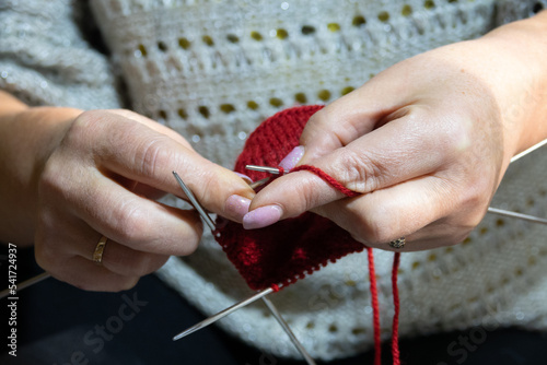 Woman hands knitting sock with needles and yarn of red color