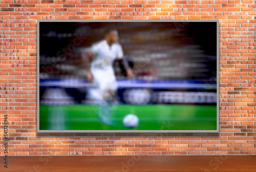 TV with soccer player on brick wall and wooden table with empty space. Selective focus. Blurred background. © JCLobo
