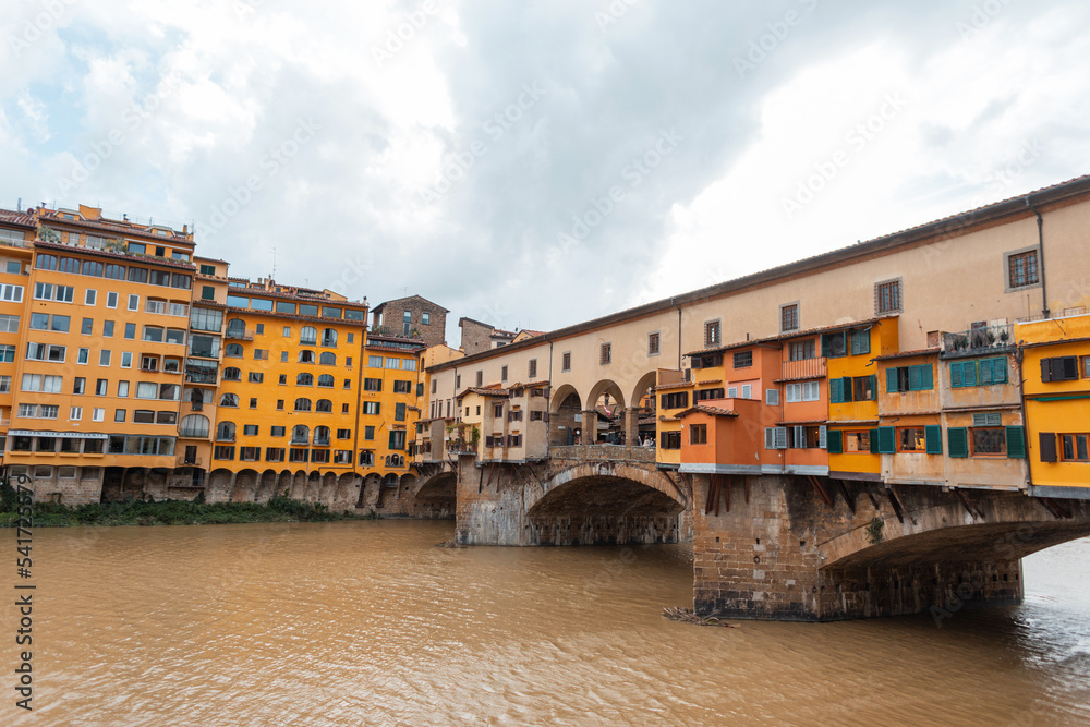 Beautiful colored yellow houses on a historic vintage bridge with a river in Florence, Italy