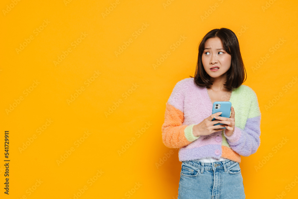 Asian displeased woman looking aside while using mobile phone Asian displeased woman looking aside while using mobile phone