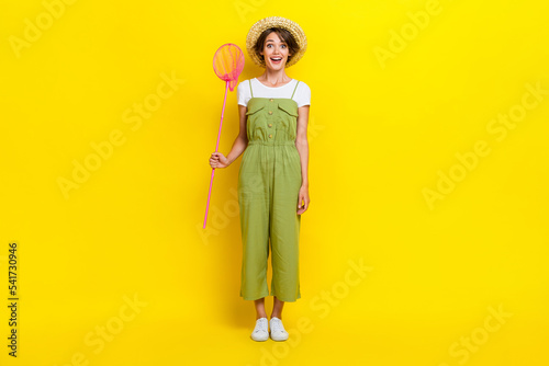 Photo of cute hair attractive carefree lady wear khaki overalls hold butterfly net excited open mouth funny cap isolated on yellow color background