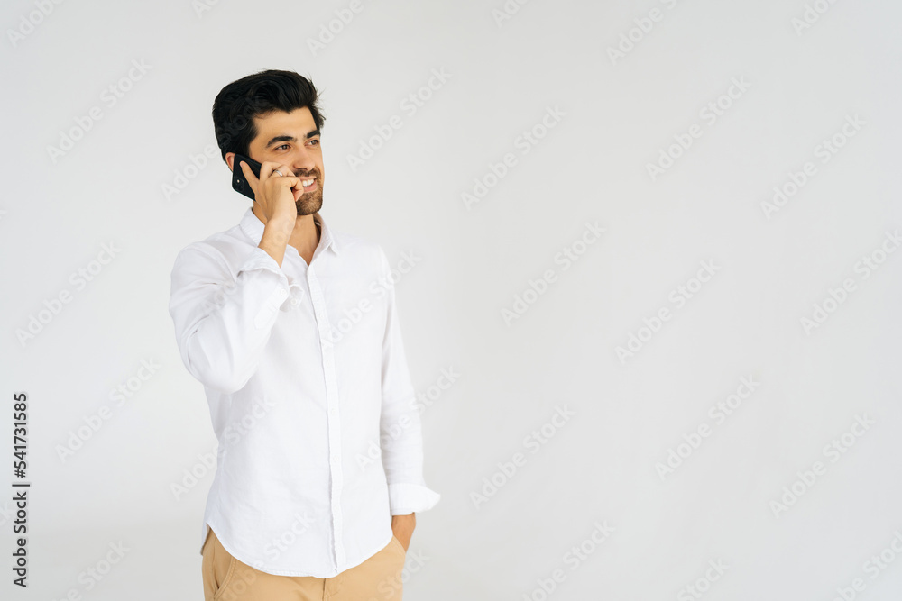 Studio portrait of smiling bearded young man talking smartphone, having conversation on mobile phone, holding and using cellphone on white isolated background, looking away. Communication concept. Studio portrait of smiling bearded young man talking smartphone, having conversation on mobile phone, holding and using cellphone on white isolated background, looking away. Communication concept.