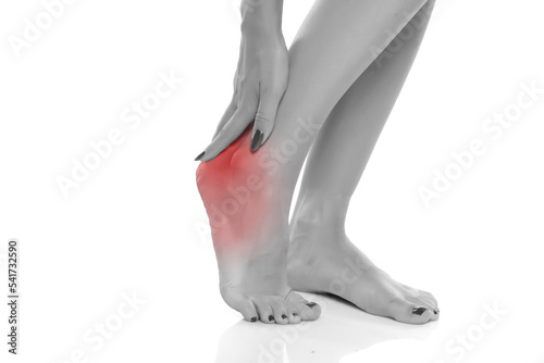 woman holding her painful heel and foot on white studio backgrou