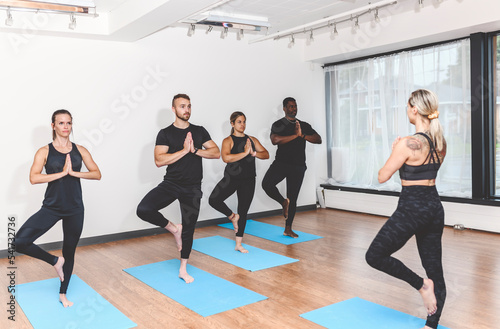 group of people with personal trainer doing yoga exercises on mats in gym