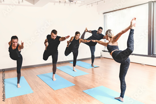 group of people with personal trainer doing yoga exercises on mats in gym