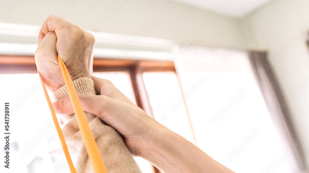 Obraz premium Close up hands of nurse caregiver using resistance band exercise for the senior patient in physiotherapy treatment. Home health care and nursing home concept.