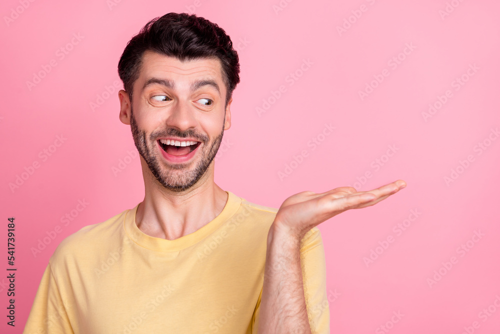 Portrait of excited astonished impressed man wear yellow t-shirt look at palm empty space open mouth isolated on pink color background Portrait of excited astonished impressed man wear yellow t-shirt look at palm empty space open mouth isolated on pink color background