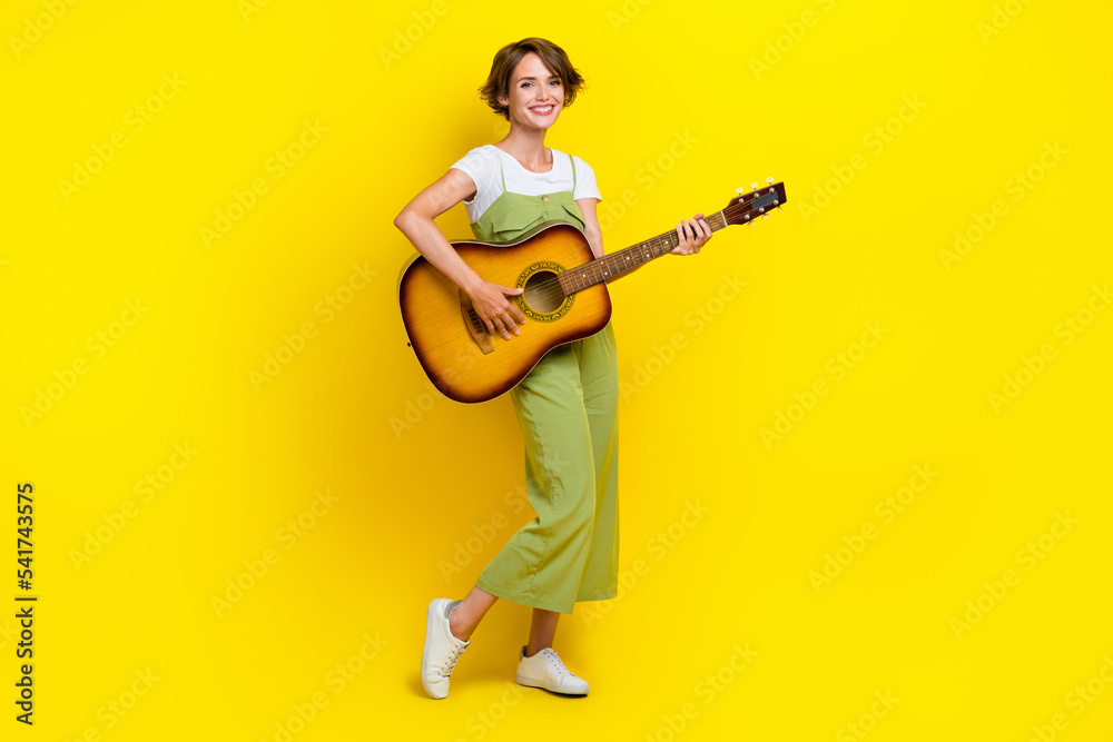 Full body photo of lovely young lady holding playing acoustic guitar dressed stylish khaki garment isolated on yellow color background Full body photo of lovely young lady holding playing acoustic guitar dressed stylish khaki garment isolated on yellow color background