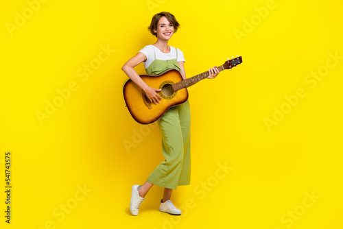 Full body photo of lovely young lady holding playing acoustic guitar dressed stylish khaki garment isolated on yellow color background